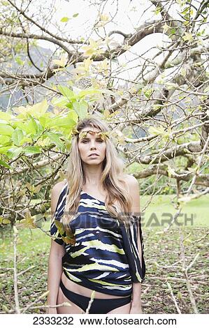 Stock Image - Portrait of a young woman with long blond hair standing in the midst of tree branches; Oahu, Hawaii, United States of America. Fotosearch