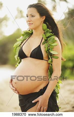 Stock Image - Pregnant Girl Wearing Black Bikini And Green Leaf Lei, Holding Tummy. Fotosearch