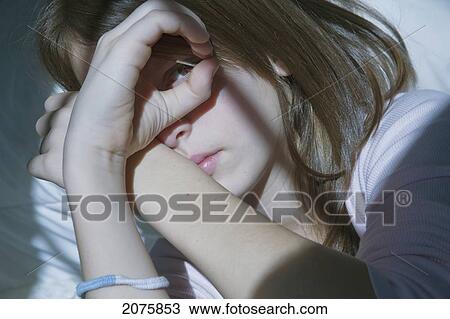 Stock Image - Preteen Girl Lying In Bed Peeking Through Her Fingers. Fotosearch