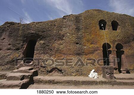 Stock Image - Priest Sitting Outside Rock Church. Fotosearch