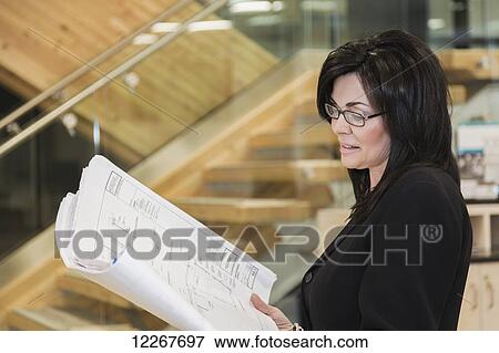 Stock Photo - Professional businesswoman reviews construction plans for new construction of office building; Edmonton, Alberta, Canada. Fotosearch