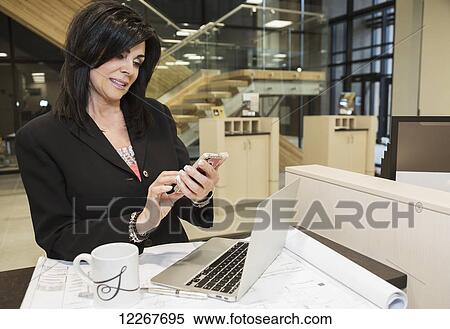 Professional businesswoman text messages while reviewing construction plans for office interior; Edmonton, Alberta, Canada View Large Photo Image Stock Photography - Professional businesswoman text messages while reviewing construction plans for office interior; Edmonton, Alberta, Canada. Fotosearch