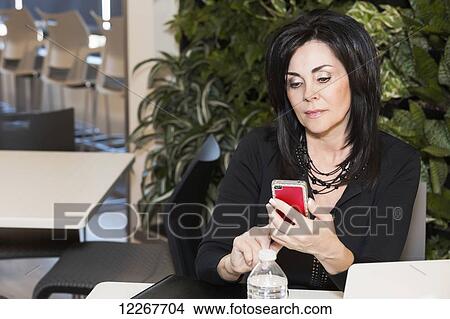 Picture - Professional businesswoman texting while taking a break in a cafeteria; Edmonton, Alberta, Canada. Fotosearch