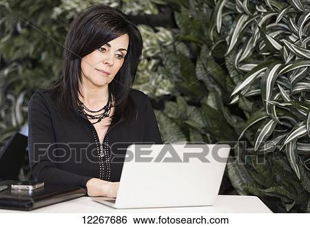 Stock Photograph - Professional businesswoman working on her laptop computer in cafeteria; Edmonton, Alberta, Canada. Fotosearch