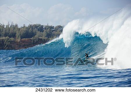 Stock Image - Professional surfer paddling into large waves at the infamous big wave spot know as Jaws or Peahi; Maui, Hawaii, United States of America. Fotosearch