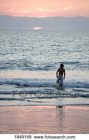 Stock Photo - Puerto Vallarta, Mexico; Young Man Wading Into Ocean At Sunset. Fotosearch