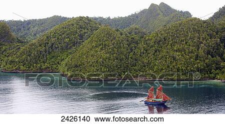 Stock Image - Pulau Wayag Islands with Tiger Blue Phinisi Schooner sailing through Raja Ampat; Indonesia. Fotosearch
