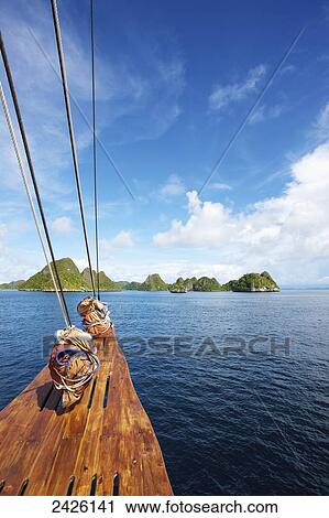 Stock Image - Pulau Wayag Islands with Tiger Blue Phinisi Schooner sailing through Raja Ampat; Indonesia. Fotosearch