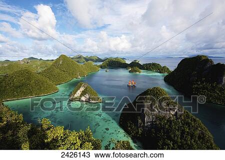 Stock Image - Pulau Wayag Islands with Tiger Blue Phinisi Schooner sailing through Raja Ampat; Indonesia. Fotosearch
