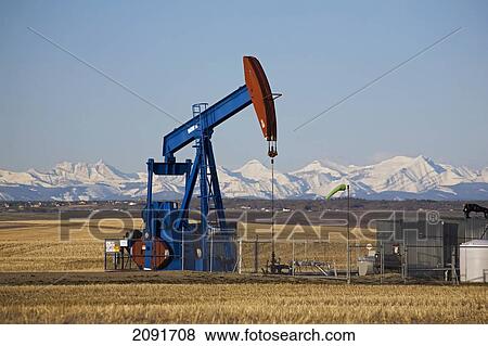Pumpjack In A Field With Snow Covered Mountains And Blue Sky In The Background; Alberta, Canada View Large Photo Image Stock Photo - Pumpjack In A Field With Snow Covered Mountains And Blue Sky In The Background; Alberta, Canada. Fotosearch