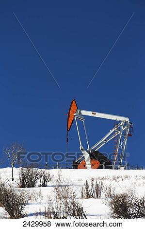 Stock Photo - Pumpjack on top of snow covered hill with blue sky; Longview, Alberta, Canada. Fotosearch