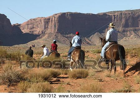 Stock Image - Rear view of horseback riders among the red rock of Monument Valley, Utah, Arizona., Utah, Arizona.. Fotosearch