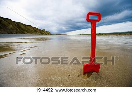Stock Image - Red Plastic Spade In Sand On Beach. Fotosearch