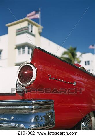 Stock Image - Red & White Ford Falcon Parked On Ocean Drive Beneath Art Deco Buildings, South Beach, Miami, Florida, Usa.. Fotosearch