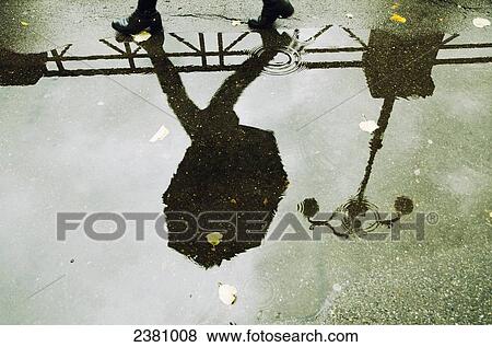 Stock Photo - Reflection in a puddle of a person walking with an umbrella and a lamp post; Locarno, Ticino, Switzerland. Fotosearch