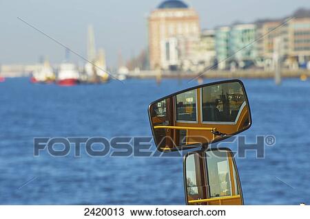 Stock Image - Reflection in the mirror of the side of a boat in the water and a view of the harbour and buildings on the shore; Hamburg, Germany. Fotosearch