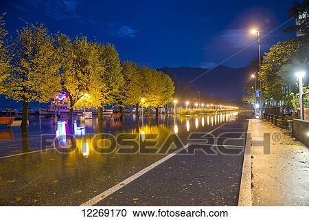 Stock Image - Reflection of lights and trees in the water due to flooding of Lake Maggiore; Locarno, Ticino, Switzerland. Fotosearch