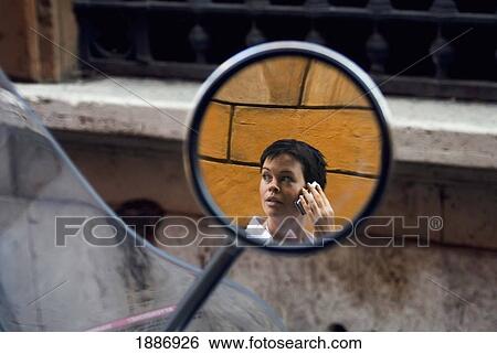 Stock Photograph - Reflection Of Woman On Mobile Phone In Scooter Mirror. Fotosearch