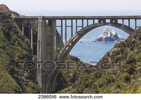 Stock Photograph - Road bridge crossing the rugged coast with a rock formation in the ocean; California, United States of America. Fotosearch