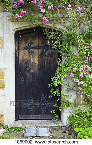 Stock Image - Roses Growing Around The Old, Wooden Door Of A Stone House. Fotosearch