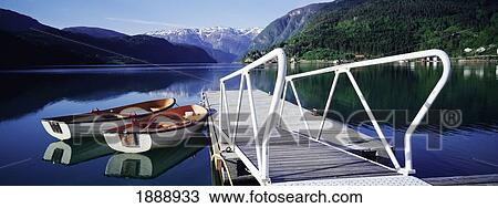 Stock Image - Row Boats By Jetty On Lake By Mountains. Fotosearch
