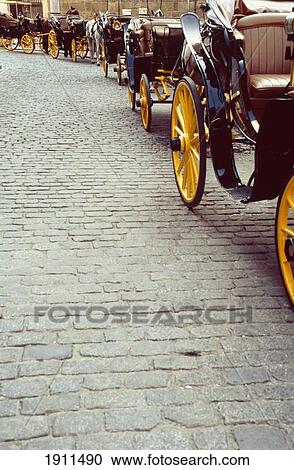 Stock Image - Row Of Horse And Carriages On Brick Road, Seville, Spain. Fotosearch