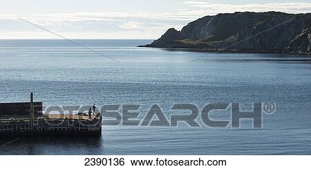 Rugged cliffs along the atlantic coastline and two people standing on a pier in the foreground; Twillingate, Newfoundland and Labrador, Canada View Large Photo Image Stock Photograph - Rugged cliffs along the atlantic coastline and two people standing on a pier in the foreground; Twillingate, Newfoundland and Labrador, Canada. Fotosearch