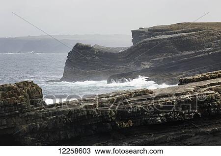Rugged dark rocky cliffs with waves and fogged sky; Kilkee, County Clare, Ireland View Large Photo Image Stock Image - Rugged dark rocky cliffs with waves and fogged sky; Kilkee, County Clare, Ireland. Fotosearch
