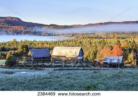 Stock Photo - Rustic buildings and barn among autumn colors at sunrise; Blanche, Outaouais, Quebec, Canada. Fotosearch