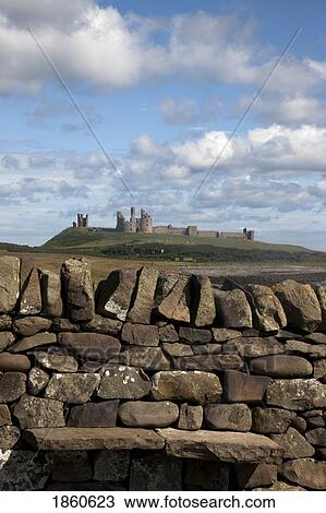 Stock Image - Rustic Stone Wall With Dunstanburgh Castle, England, Northumberland. Fotosearch