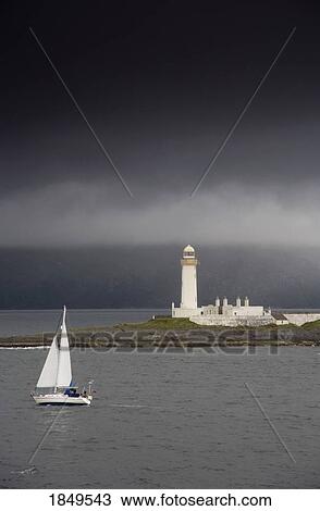 Stock Image - Sailboat Near A Shore With A Lighthouse; Eilean Musdile In The Firth Of Lorn, Scotland. Fotosearch