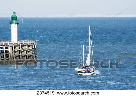 Stock Photo - Sailboat sailing by the lighthouse; Calais, France. Fotosearch