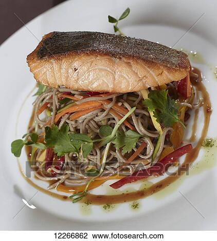 Stock Image - Salmon atop noodles and julienne carrots and red peppers in a Thai sauce garnished with parsley; Ontario, Canada. Fotosearch
