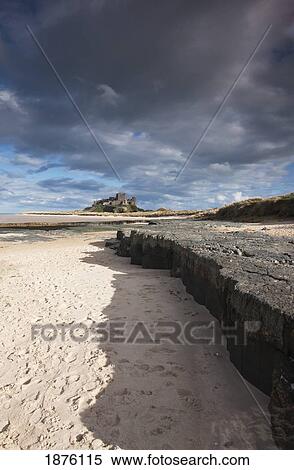 Stock Photography - Sand Along A Rock Ledge With Dark Clouds In The Sky; Bamburgh, Northumberland, England. Fotosearch