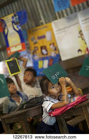 Stock Image - Schoolgirl holding chalkboard upside down in the classroom; Phnom Penh, Cambodia. Fotosearch