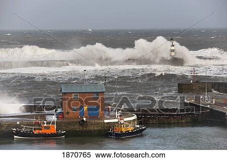 Stock Photography - Seaham, Teesside, England; Waves Crashing Into A Lighthouse And Boats Along A Pier. Fotosearch