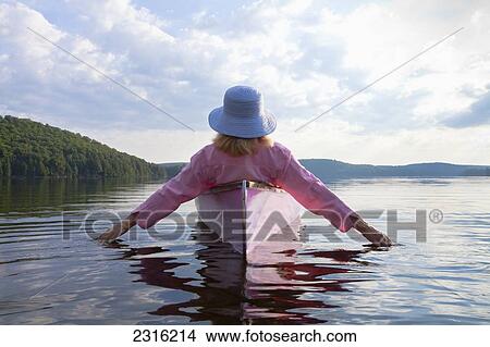 Picture - Senior Woman Dressed In Pink And Trailing Her Hands In The Water From Her Pink Canoe In Algonquin Park; Ontario Canada. Fotosearch