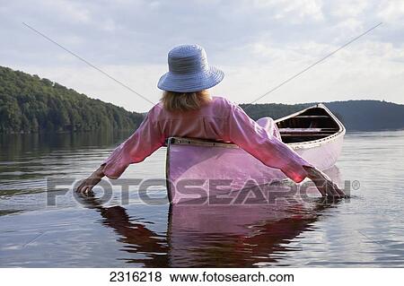 Stock Photo - Senior Woman Dressed In Pink And Trailing Her Hands In The Water From Her Pink Canoe In Algonquin Park; Ontario Canada. Fotosearch