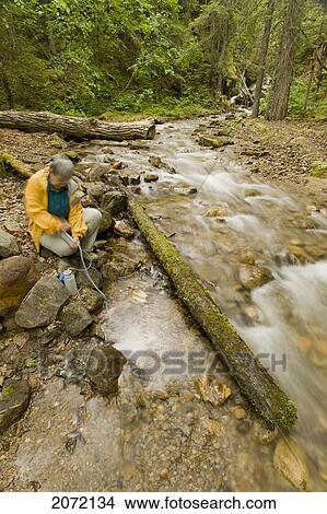 Picture - Senior Woman Filtering Water For Drinking In A Creek On The Chilkoot Trail, Yukon. Fotosearch