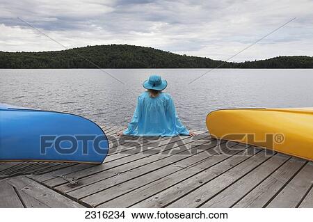 Senior Woman Sitting On A Dock Between Her Canoes Under A Stormy Sky In Algonquin Park; Ontario Canada View Large Photo Image Picture - Senior Woman Sitting On A Dock Between Her Canoes Under A Stormy Sky In Algonquin Park; Ontario Canada. Fotosearch