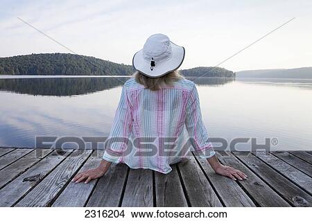 Senior Woman Sitting On Her Cottage Dock Looking Out At Lake In Algonquin Park; Ontario Canada View Large Photo Image Picture - Senior Woman Sitting On Her Cottage Dock Looking Out At Lake In Algonquin Park; Ontario Canada. Fotosearch