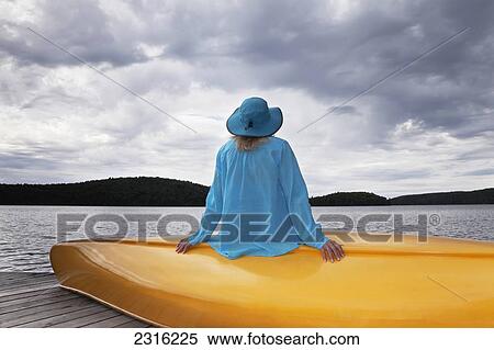 Stock Photography - Senior Woman Sitting On Her Yellow Canoe And Looking Up At A Stormy Sky In Algonquin Park; Ontario Canada. Fotosearch