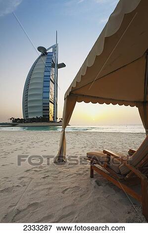 Stock Photo - Shaded Chairs On Beach In Front Of The Burj Al Arab At Dusk; Dubai, United Arab Emirates. Fotosearch