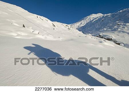 Stock Photograph - Shadow of walker with rucksack going up snowy slopes of Beinn Respiol, Ardnamurchan peninsula; Highlands, Scotland. Fotosearch