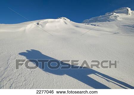 Stock Photograph - Shadow of walker with rucksack going up snowy slopes of Beinn Respiol, Ardnamurchan peninsula; Highlands, Scotland. Fotosearch