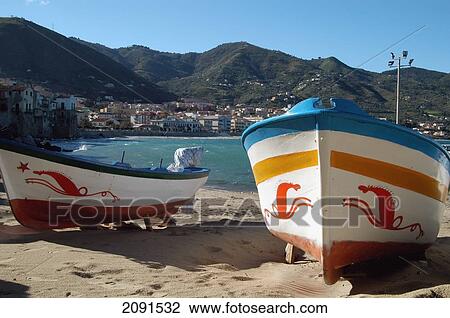 Stock Image - Sicily, Italy: Boats Decorated With Traditional Sea-Horse Motifs On The Small Beach In The Harbour In The Old Town Of Cefalu. Copyright.. Fotosearch