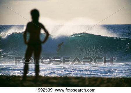 Stock Photo - Sihouette Of Person Standing On The Beach At Pipeline Watching Surfer On Big Wave.. Fotosearch
