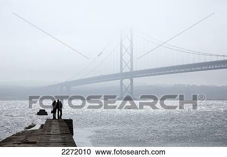 Silhouette Of A Couple Standing At The End Of A Wooden Pier Looking Out Over The Water At A Bridge In The Fog; North Queensferry Fife Scotland View Large Photo Image Stock Image - Silhouette Of A Couple Standing At The End Of A Wooden Pier Looking Out Over The Water At A Bridge In The Fog; North Queensferry Fife Scotland. Fotosearch