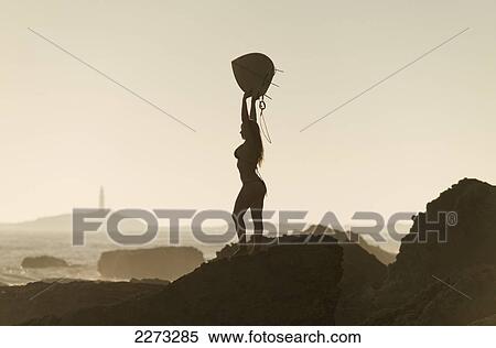 Silhouette of a female surfer holding her surfboard up above her head while standing on a rock at the coast; andalusia spain View Large Photo Image Stock Photography - Silhouette of a female surfer holding her surfboard up above her head while standing on a rock at the coast; andalusia spain. Fotosearch