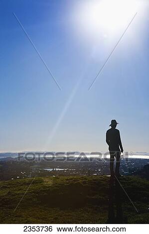 Stock Photograph - Silhouette Of A Man In A Hat Standing On Mt. Eden With A View Of Auckland; New Zealand. Fotosearch